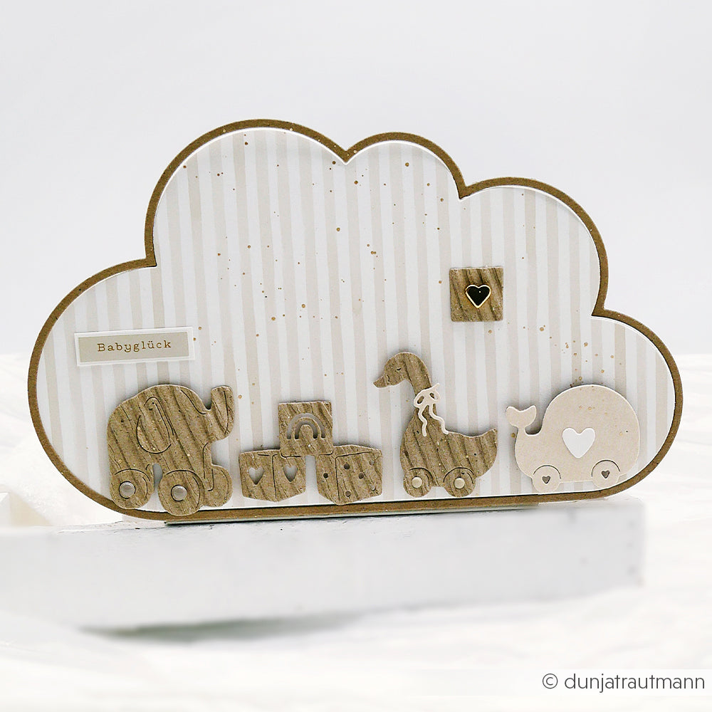 Holzspielzeug und -klötze ruhen auf einem wolkenförmigen Hintergrund von Streifen warmgrau Designpapier von Alexandra Renke, das mit einem Babyglück-Label versehen ist.