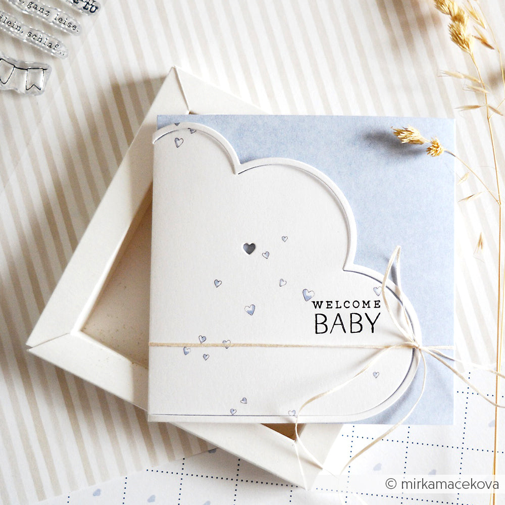 Quadratische Karte von Alexandra Renke mit Wolkenform, "Welcome Baby"-Text, blauen Herz-Akzenten (Designpapier Herzchen hellblau) und Bindfaden auf einer offenen Schachtel - ein charmantes Stück Buchbinderei für einzigartige Papierprojekte.