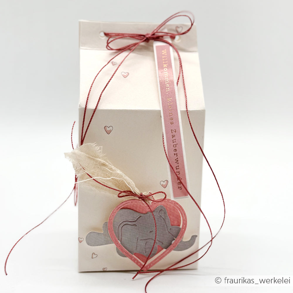 Cremefarbene Geschenkbox von Alexandra Renke mit Herz- und Elefantenmotiven, gebunden mit roter Kordel und Stoffdetail - ideal für Papierprojekte oder Buchbinderei, akzentuiert durch entzückende Designpapier Herzchen rosa Elemente.