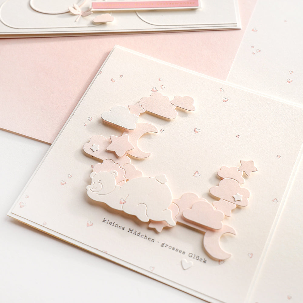 Eine pastellfarbene Karte von Alexandra Renke mit Wolken, Sternen, einem schlafenden Bären und dem Text "kleines Mädchen - grosses Glück", hergestellt mit Designpapier Herzchen rosa - ideal für Papierprojekte oder Buchbinderei-Geschenke.