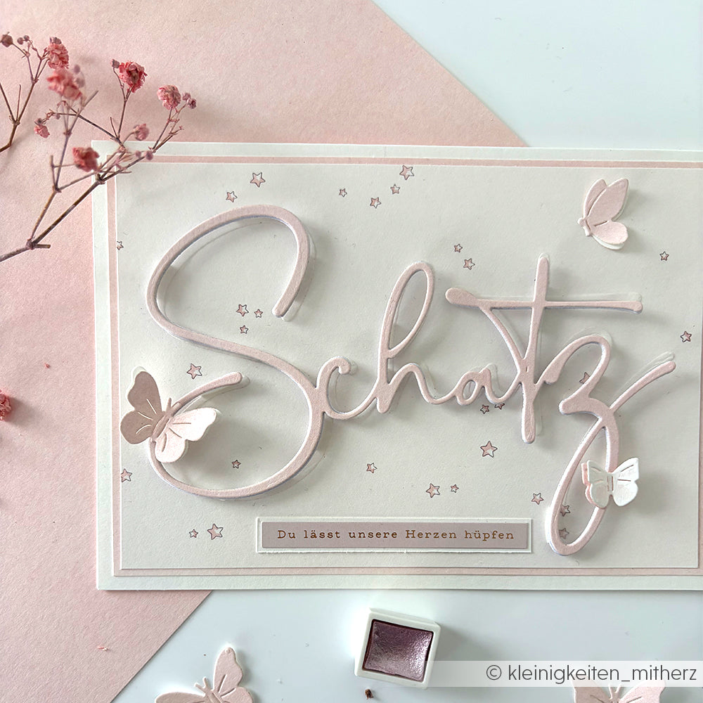 Alexandra Renke Grußkarte mit "Schatz" in Schreibschrift, Schmetterlingen, Sternen und rosa Details auf Designpapier Sternenhimmel hellrosa-ideal für Papierprojekte oder Buchbinderei. Text: Du lässt unsere Herzen hüpfen.