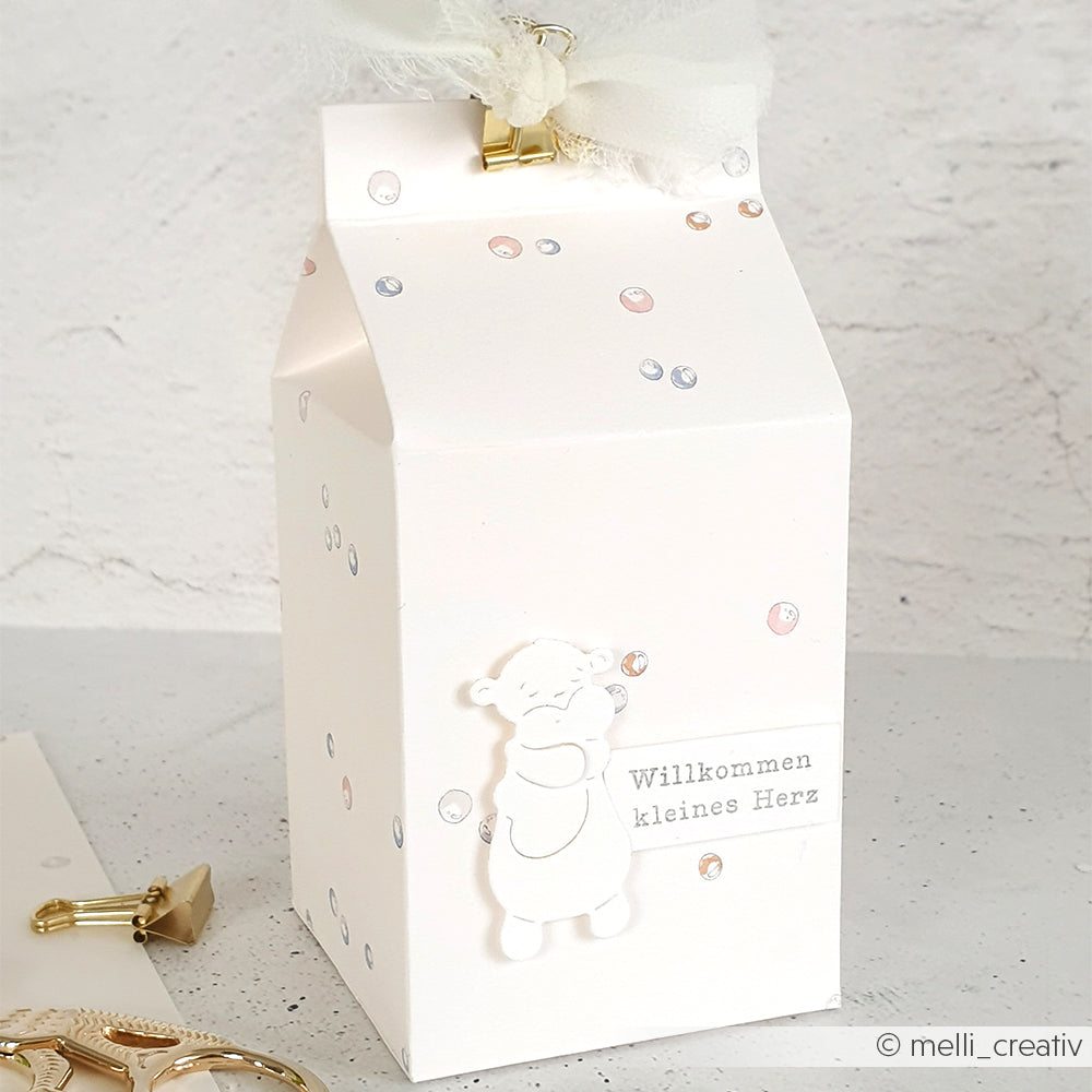 Die weiße Geschenkbox in Form einer Milchtüte von Alexandra Renke ist mit einem Bären und dem Schriftzug "Willkommen kleines Herz" verziert - ideal für Papierprojekte oder Geschenke der Buchbinderei.