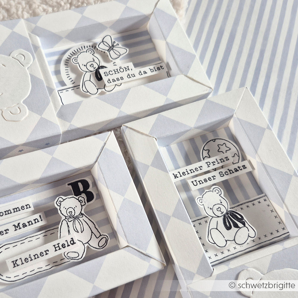 Drei weiß-graue Grußkarten von Alexandra Renke mit Teddybär-Illustrationen und deutschem Text auf Designpapier von Große Karo Feenblau werden auf einer gestreiften Fläche präsentiert.