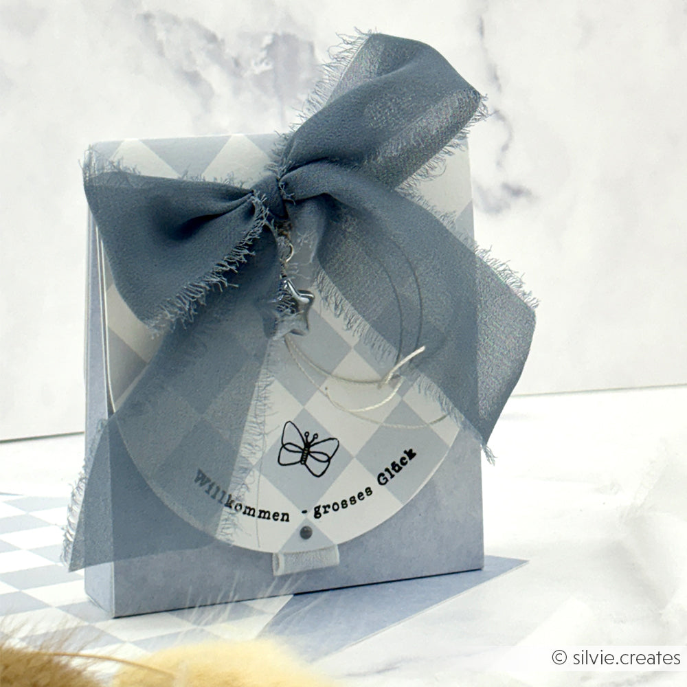 Eine Geschenkbox von Alexandra Renke mit blauer Schleife und Sternanhänger aus Metall, hergestellt aus Designpapier Große Karo Feenblau-ideal für Papierprojekte. Beschriftet mit "Willkommen - großes Glück.