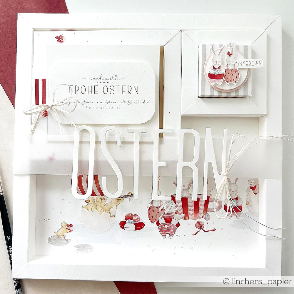 Gerahmte Osterbastelei von Alexandra Renke mit OSTERN-Schriftzug, Hasen, Eiern und festlichen rot-weißen Motiven - ideal für Papierprojekte oder zum Dekorieren von Grußkarten mit dem charmanten Designpapier Ostern.