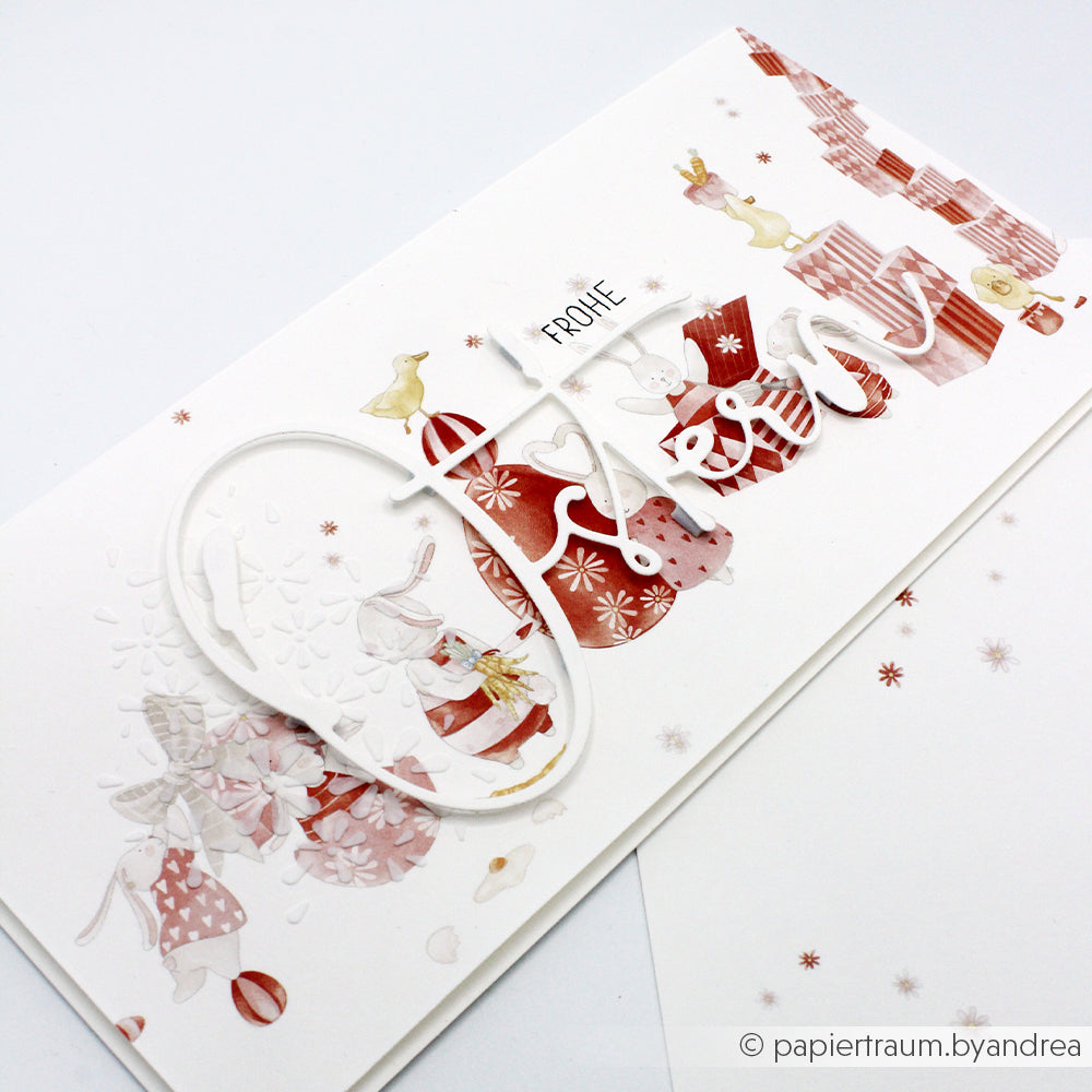 Festliche Weihnachtskarte von Alexandra Renke mit roten und weißen Geschenken, Hasen und dem Gruß "Frohe Ostern" auf hochwertigem Designpapier - ideal für Ihre Papierprojekte oder Buchbinderei-Kreationen.