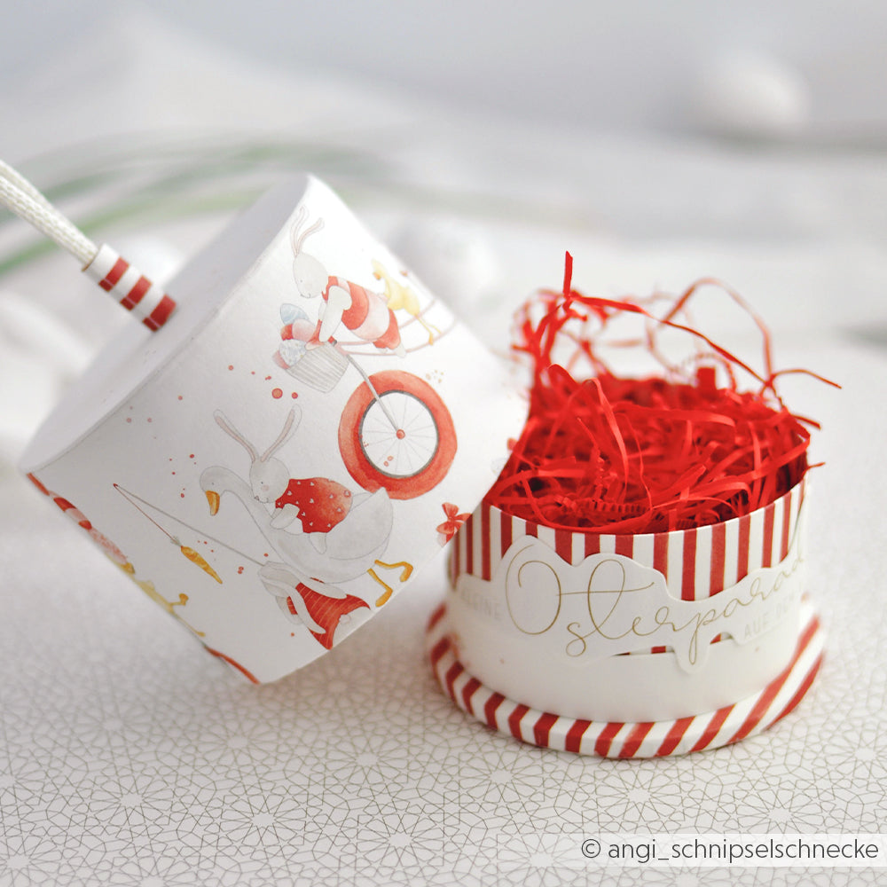 Runde Geschenkbox mit rotem geschreddertem Papier, verziert mit Enten und roten Streifen mit Alexandra Renke Designpapier Osterparade-ideal für Papierprojekte. Der Deckel wird neben die Schachtel gelegt.