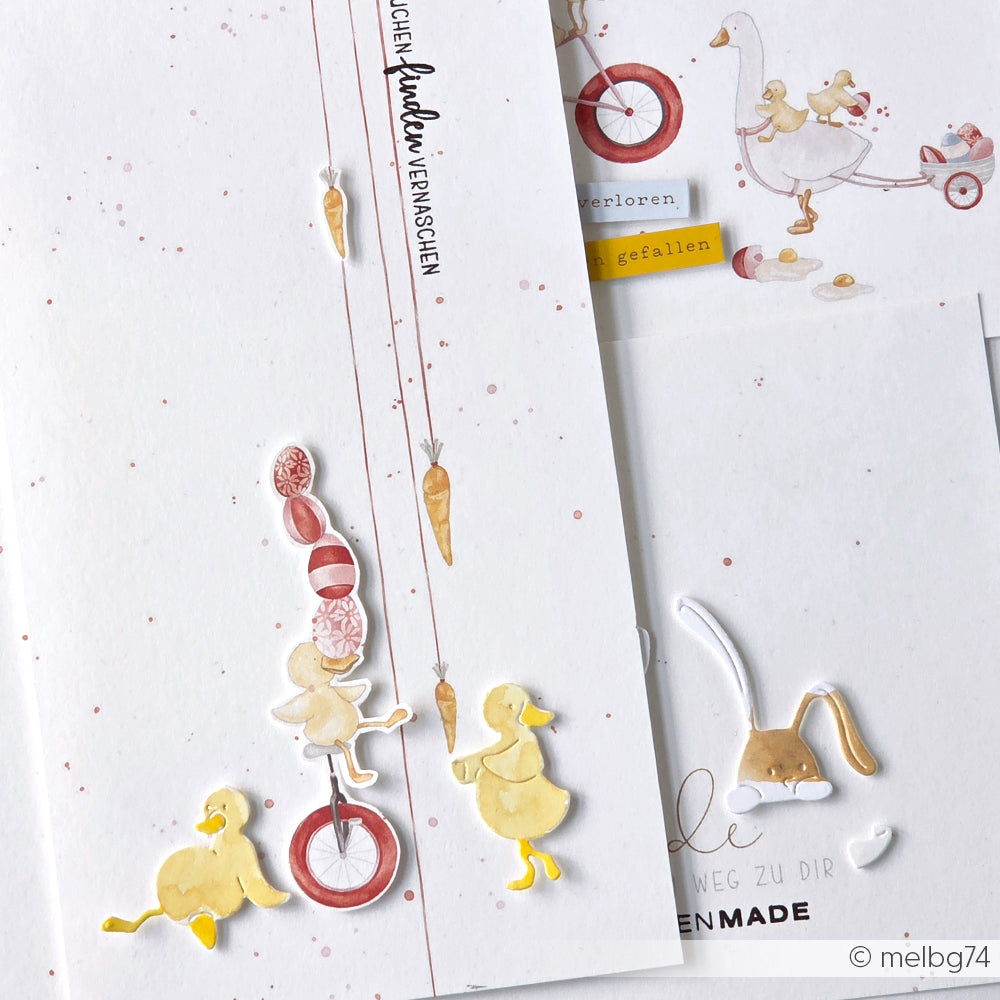 Drei illustrierte Enten balancieren auf einem Einrad unter einer Karotte, mit verspielten Alexandra Renke Details und Osterparade Designpapier - die perfekte Inspiration für Ihr nächstes Papierprojekt!.
