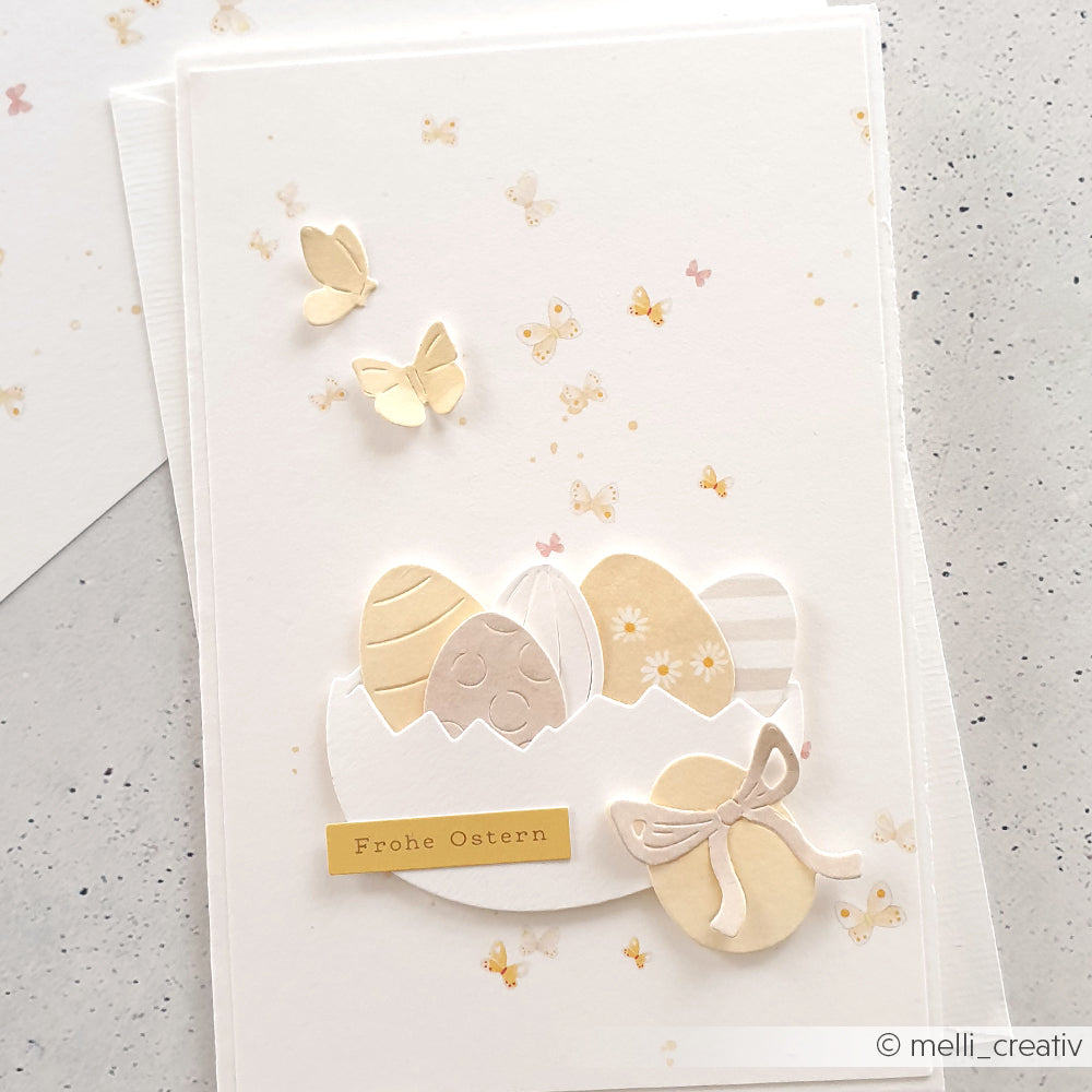 Handgemachte Osterkarte von Alexandra Renke mit pastellfarbenen Eiern, Schmetterlingsreigen, einer Schleife und "Frohe Ostern"-Text auf hochwertigem Designpapier. Perfekt für Liebhaber von Papierprojekten.