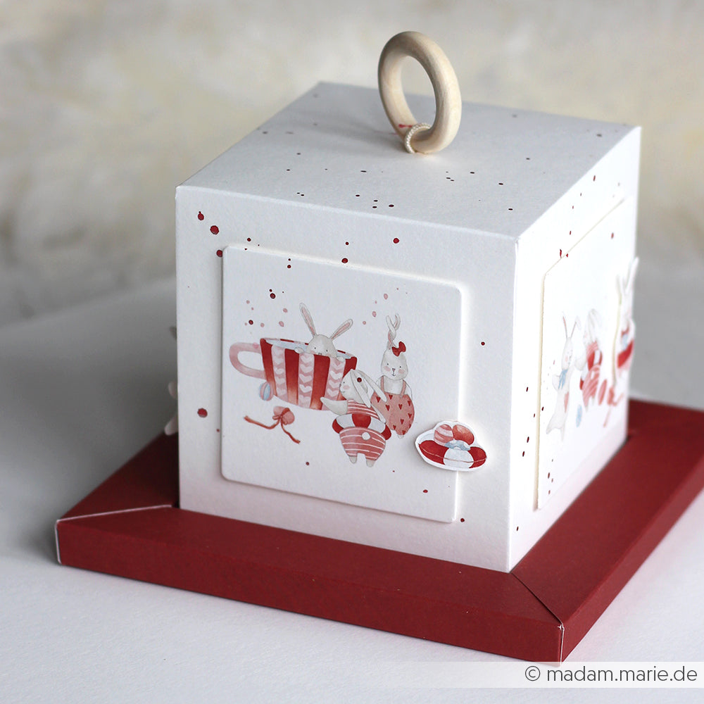 Bezaubernde weiße Schachtel von Alexandra Renke mit roten Akzenten, Hasenillustrationen, einem hölzernen Ringgriff und tollem Designpapier - ideal für Papierprojekte oder Buchbinderei.