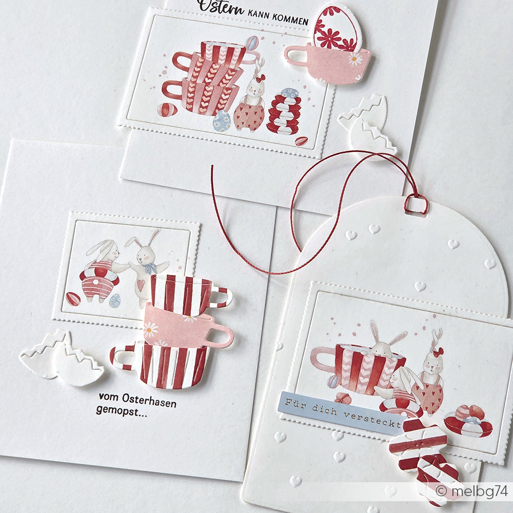 Handgefertigte Ostergrußkarten von Alexandra Renke zeigen rot gestreifte Tassen, Hasen, Herzen und deutsche Grüße auf weißem Designpapier - perfekt für Ihre Papierprojekte.