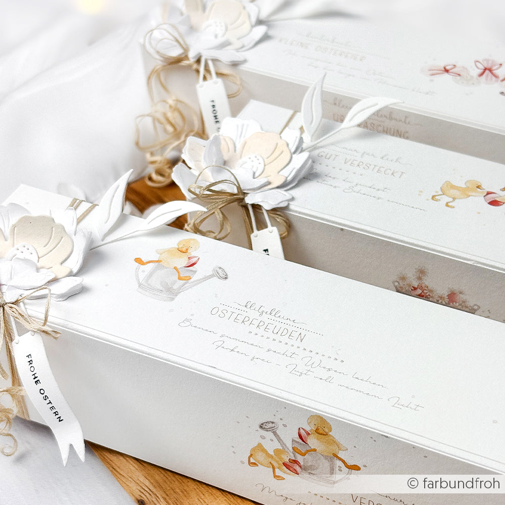 Elegante weiße Ostergeschenkboxen von Alexandra Renke, verziert mit floralen Designpapier-Anhängern, Schleifenband und illustrierten Hasen und Küken - ideal für Papierprojekte oder zur Kombination mit passenden Grußkarten.