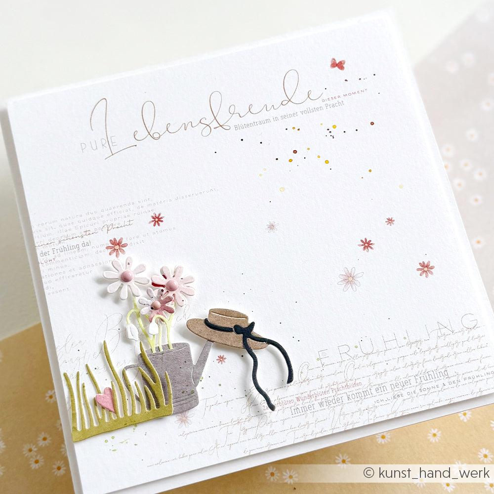 Handgemachte Karte von Alexandra Renke mit Papierblumen, einem Hut, Gras und rosa Akzenten auf feinem Designpapier. Inklusive deutschem Text auf weißem Hintergrund - ideal für einzigartige Papierprojekte.
