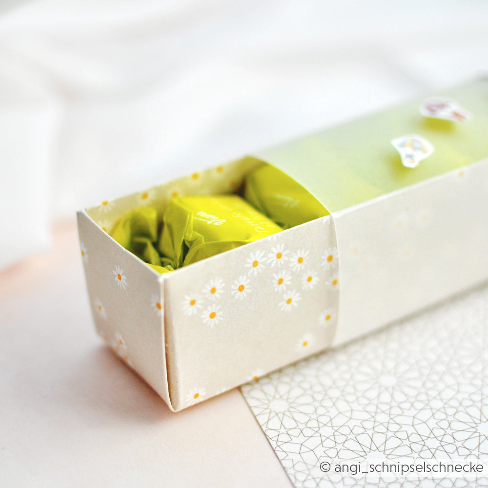 Rechteckige Schachtel von Alexandra Renke mit margeritenreigen Gänseblümchen-Motiv, teilweise geöffnet, um ein gelb-grün verpacktes Bonbon zu zeigen - ideal für schicke Papierprojekte oder zum Verschenken besonderer Leckereien.