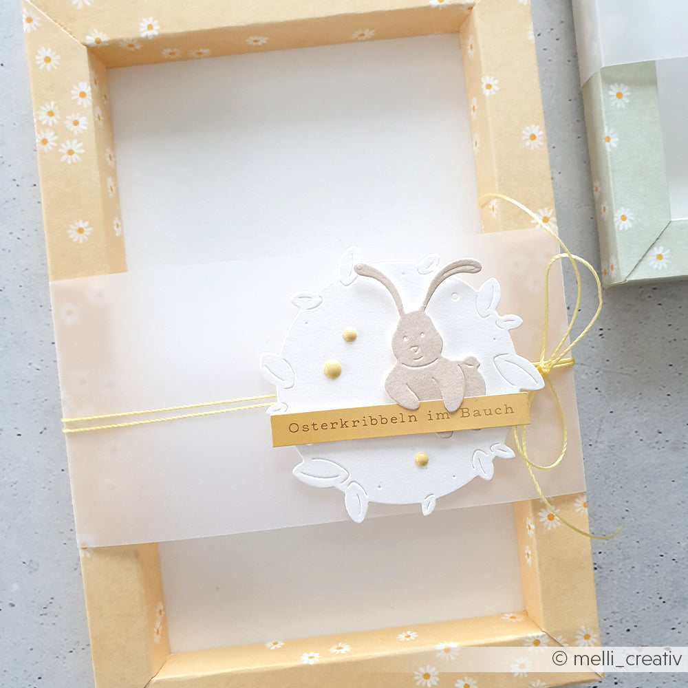 Das Designpapier Margeritenreigen auf Gelb von Alexandra Renke bietet einen gelben Blumenrahmen, eine Karte mit Hase und den Text "Osterkribbeln im Bauch" - ideal für charmante Papierprojekte auf weißem Hintergrund.