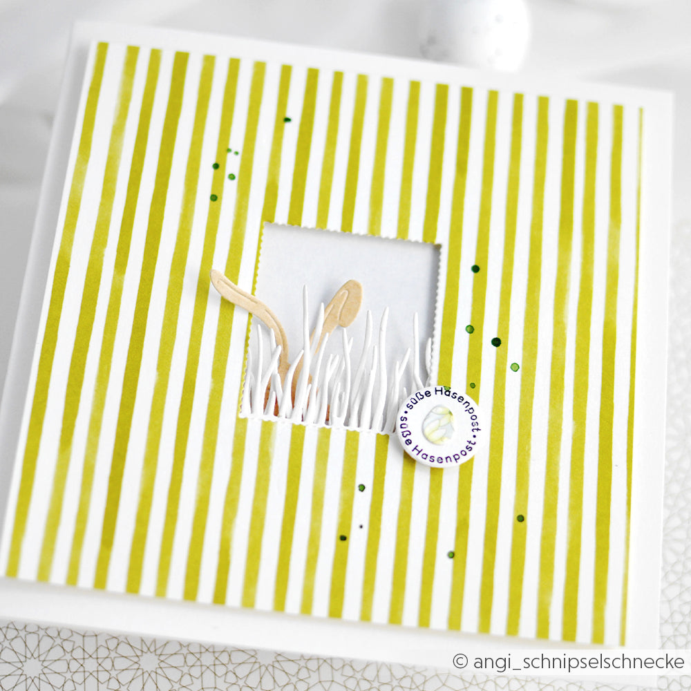 Quadratische Karte von Alexandra Renke, hergestellt aus Designpapier Streifen Chartreuse mit grünen Streifen, einem Fenster mit weißem Gras und einem runden deutschen Etikett - perfekt für Buchbinderei oder kreative Papierprojekte.