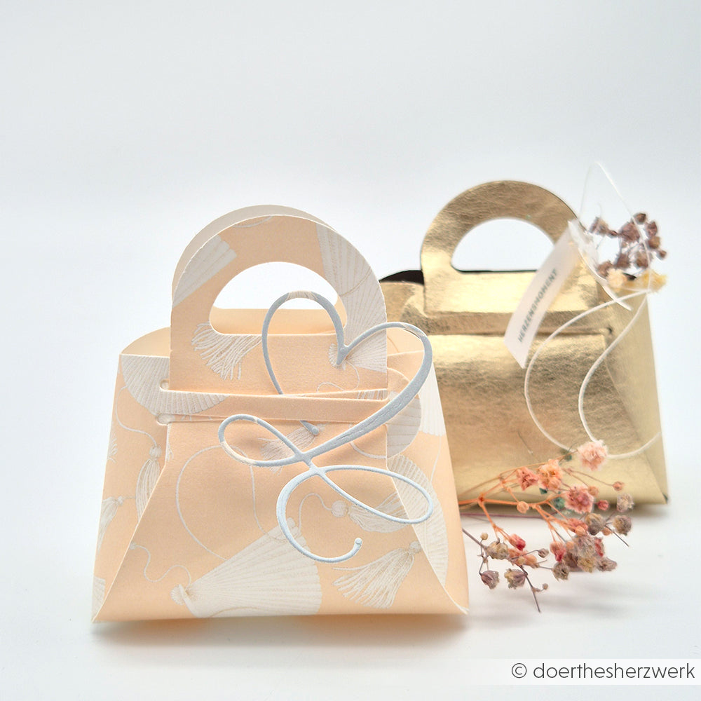 Zwei dekorative Geschenktaschen von Alexandra Renke, eine pfirsichfarbene mit Herzklammer, eine goldene aus feinem Designpapier, sind mit getrockneten Blumen bestückt, ideal für Grußkarten oder andere Papierarbeiten.