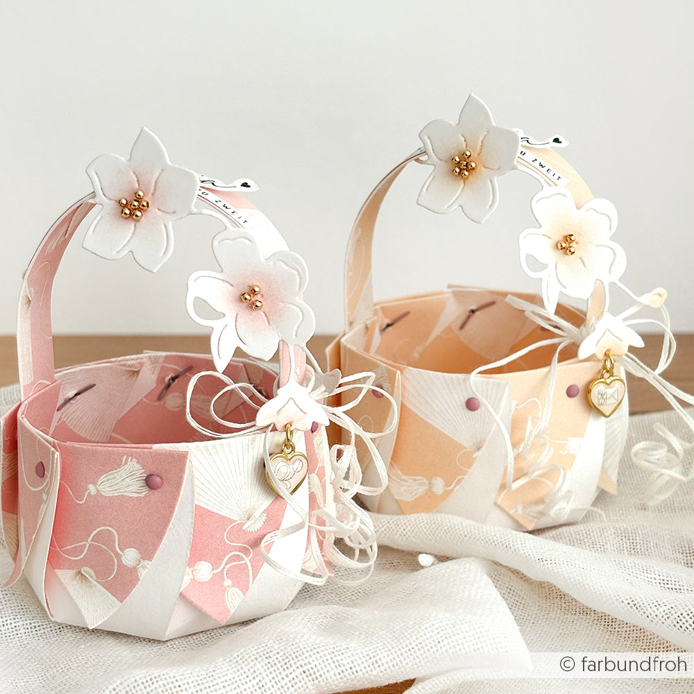 Zwei pastellfarbene Körbe mit floralen Henkeln, Herzanhängern und Schleifenband auf leichtem Stoff - perfekt für Papierprojekte oder in Kombination mit Grußkarten und Designpapier von Alexandra Renke.
