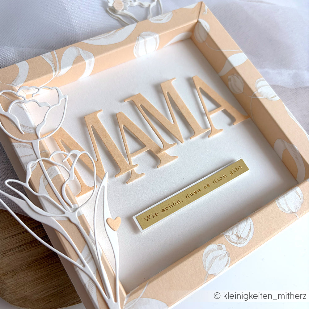 Schattenbox von Alexandra Renke mit "MAMA", floralen Motiven auf Designpapier Tulpen auf Elegant-Marille, dazu ein goldenes Etikett "Wie schön, dass es dich gibt" - eine schöne Ergänzung zu Ihren Papierprojekten.