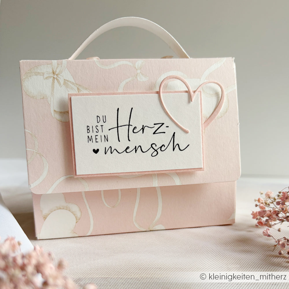 Die rosafarbene Geschenktasche von Alexandra Renke ist mit einem Herz und dem Schriftzug "Du bist mein Herzmensch" versehen. Sie ist aus Designpapier mit zarten Herzen auf Rosa gefertigt - ideal für Papierprojekte oder als charmante, herzliche Geschenktasche.