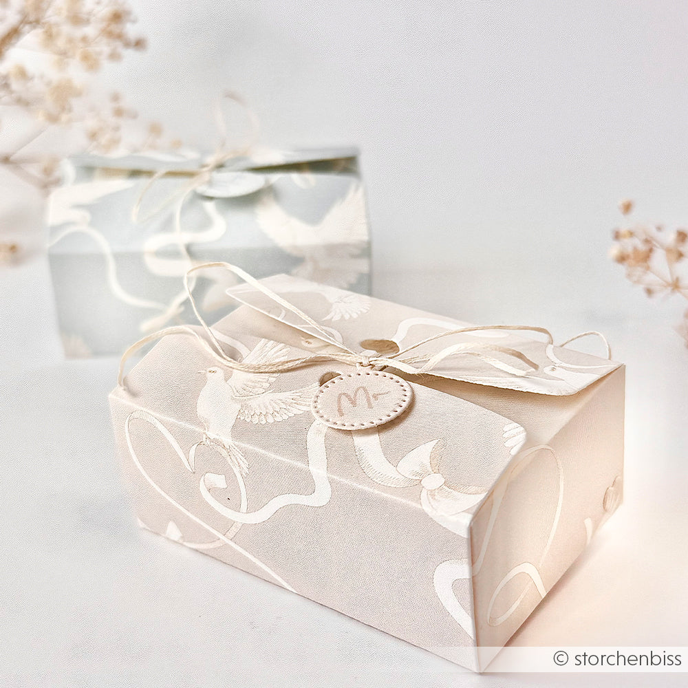Zwei elegante weiße Geschenkschachteln von Alexandra Renke mit zarten Vogelmotiven und Schleifenband auf hochwertigem Designpapier auf hellem Hintergrund.