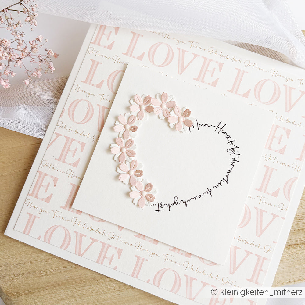 Quadratische Karte von Alexandra Renke mit rosa Papierblumen in Herzform, umgeben von dem Wort LOVE - ideal für Papierprojekte oder zur Verschönerung Ihrer nächsten Designpapier-Kreation.