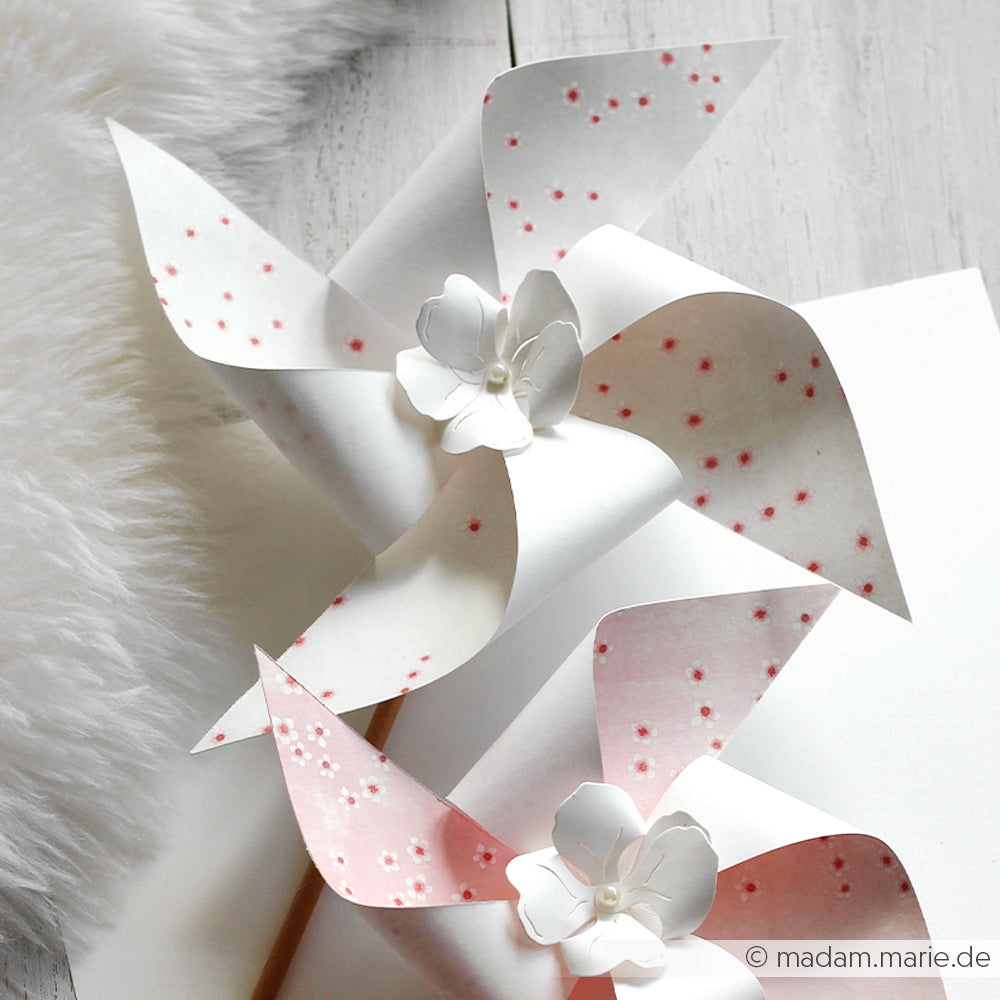 Zwei Papier-Pinwheels mit rosa Blumenmustern aus Alexandra Renke Designpapier Kirschblüten und weißen Papierblumen auf weißem Untergrund, perfekt für kreative Papierprojekte oder als charmante Buchbinderei-Verzierungen.