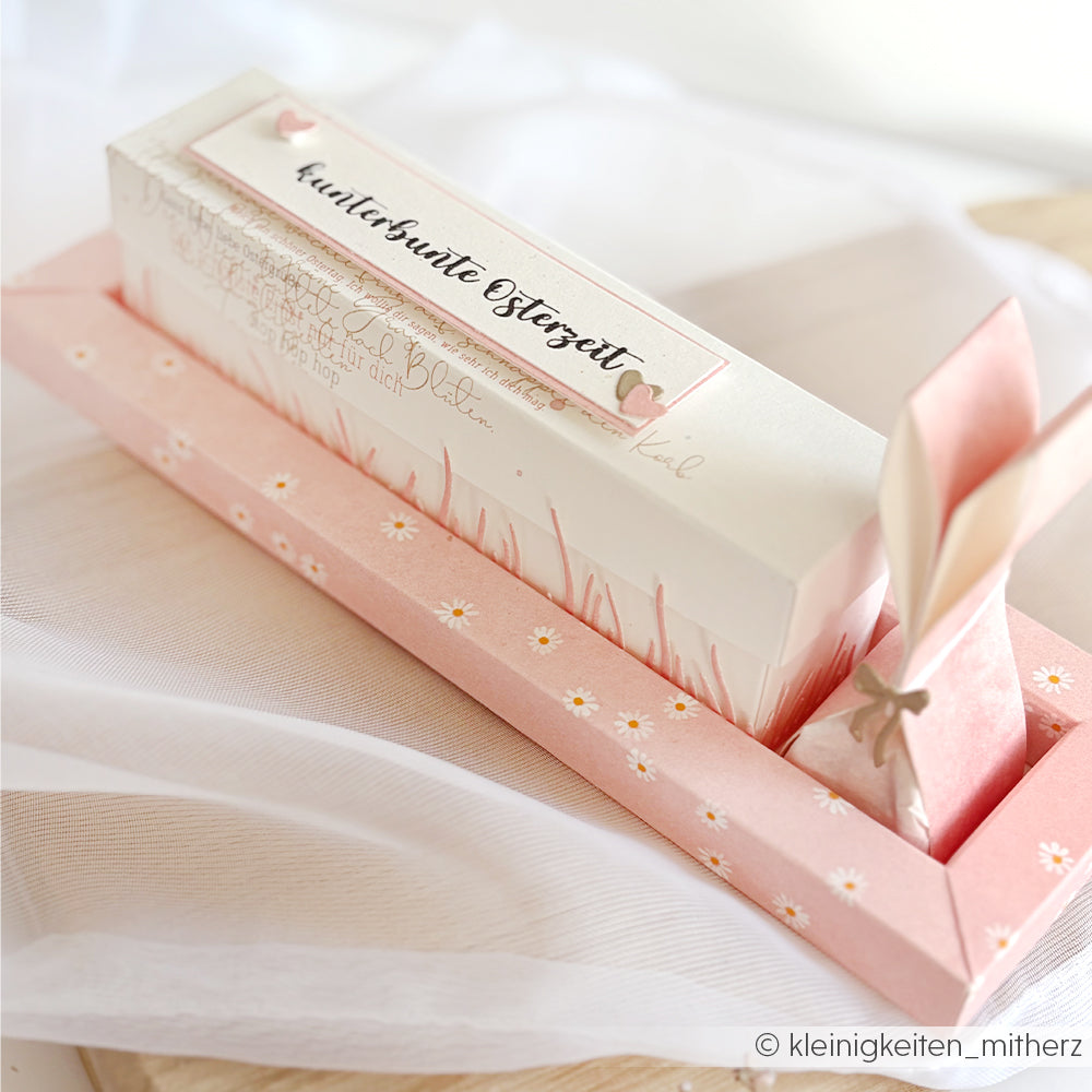 Rechteckige pastellfarbene Geschenkbox von Alexandra Renke mit deutschem Text, floralem Designpapier und einer gefalteten Hasenfigur auf einem Tablett - ideal für Papierprojekte oder zur Präsentation von Lieblingsblüten.