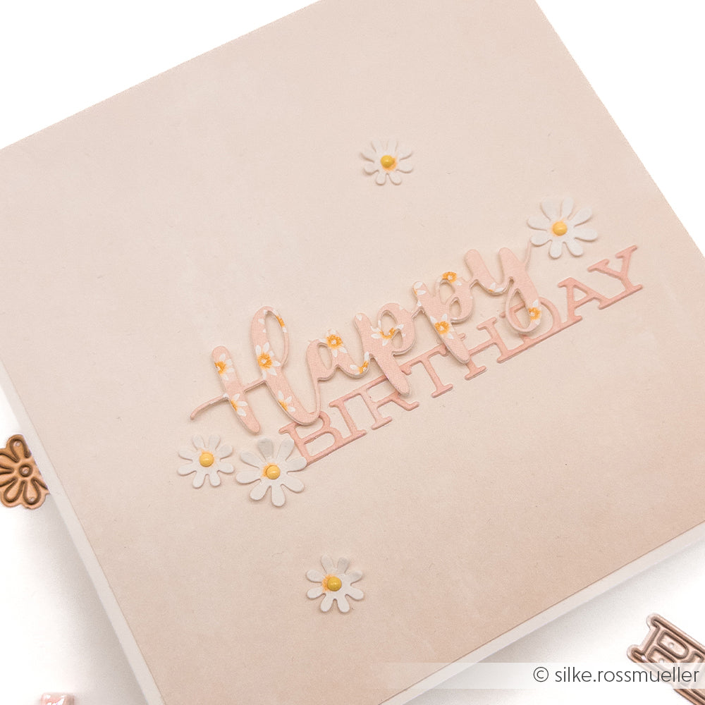 Quadratische Karte von Alexandra Renke mit "Happy Birthday" in rosa Buchstaben und kleinen weißen Gänseblümchen auf einem hellbeigen Designpapier-Hintergrund - ideal für Papierprojekte oder zum Feiern Ihrer Lieblingsblüten zu besonderen Anlässen.
