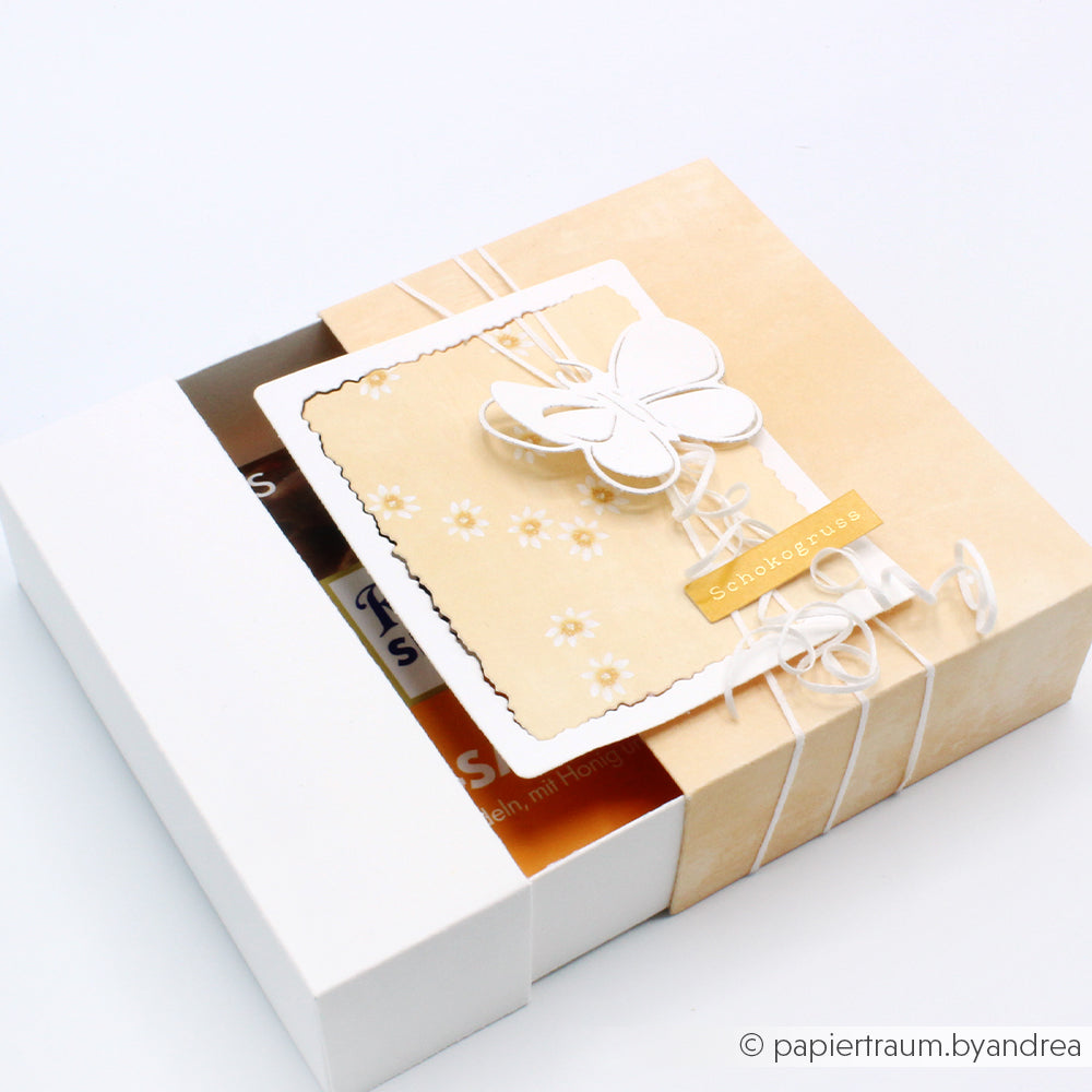 Eine cremefarbene und weiße Geschenkbox von Alexandra Renke, die mit warmem apricotfarbenem Designpapier gestaltet wurde, enthält eine Schmetterlingskarte und Lieblingsblüten, die sich teilweise öffnen lassen, um die Schokoladentafeln im Inneren zu zeigen.