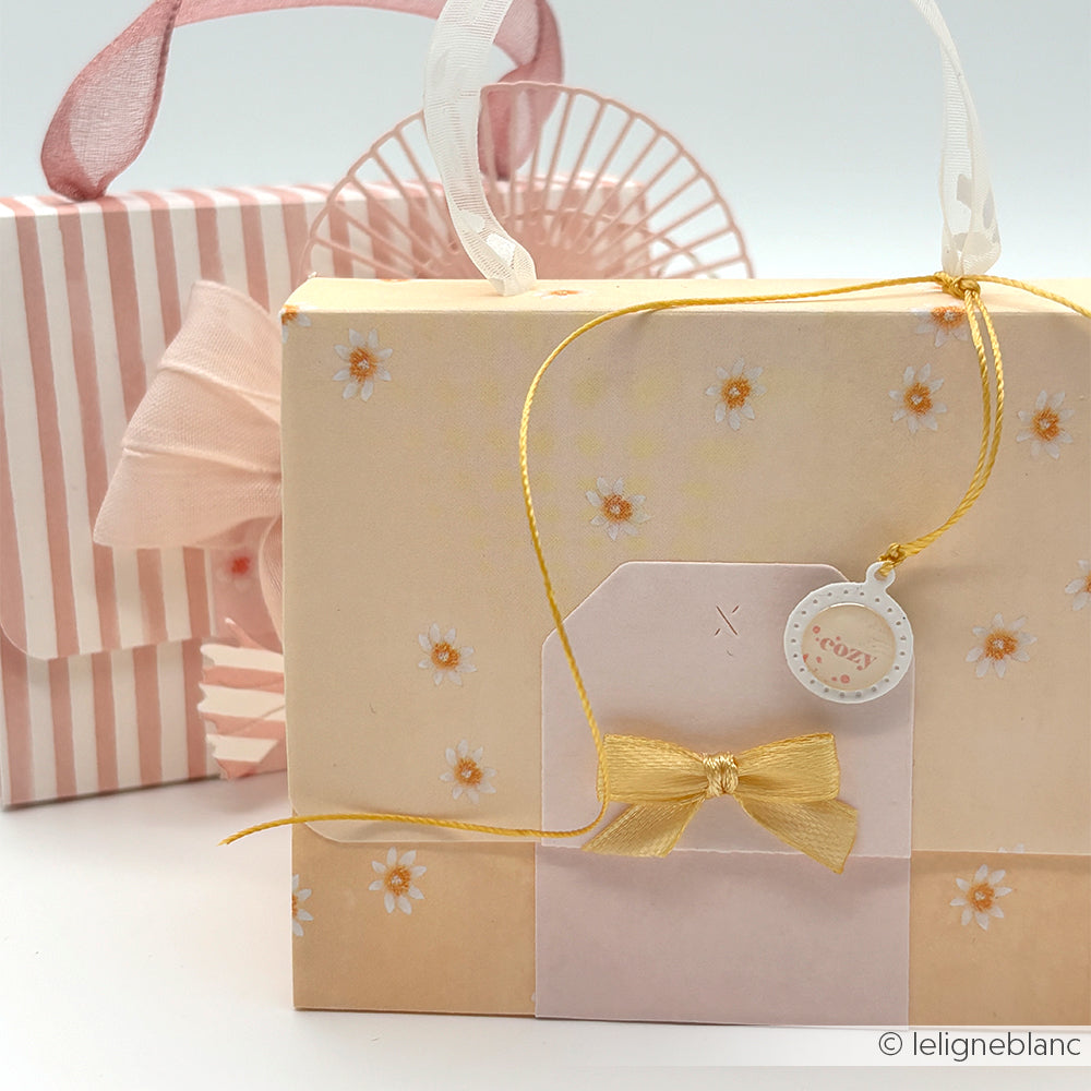 Alexandra Renke pastellfarbene Geschenktüten mit Schleifen und floralen Mustern, mit Lieblingsblüten auf Warmapricot Designpapier; eine davon enthält einen "gemütlichen" Anhänger und eine goldene Schnur. Ideal für Papierprojekte. Ausgestellt auf weißem Hintergrund.