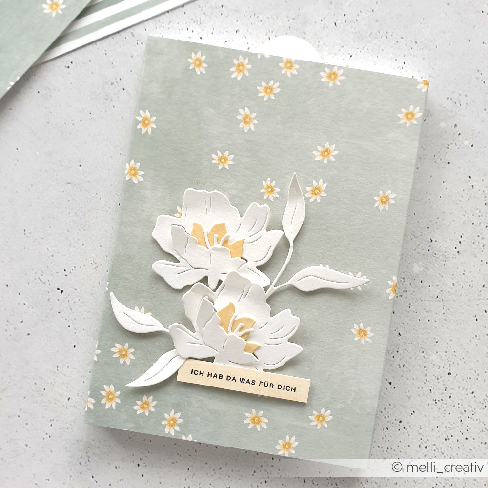 Die florale Grußkarte von Alexandra Renke zeigt Lieblingsblüten auf Sagegrün mit weißen Blumen, Gänseblümchen und dem Aufkleber "ICH HAB DA WAS FÜR DICH" - ideal für besondere Papierprojekte.
