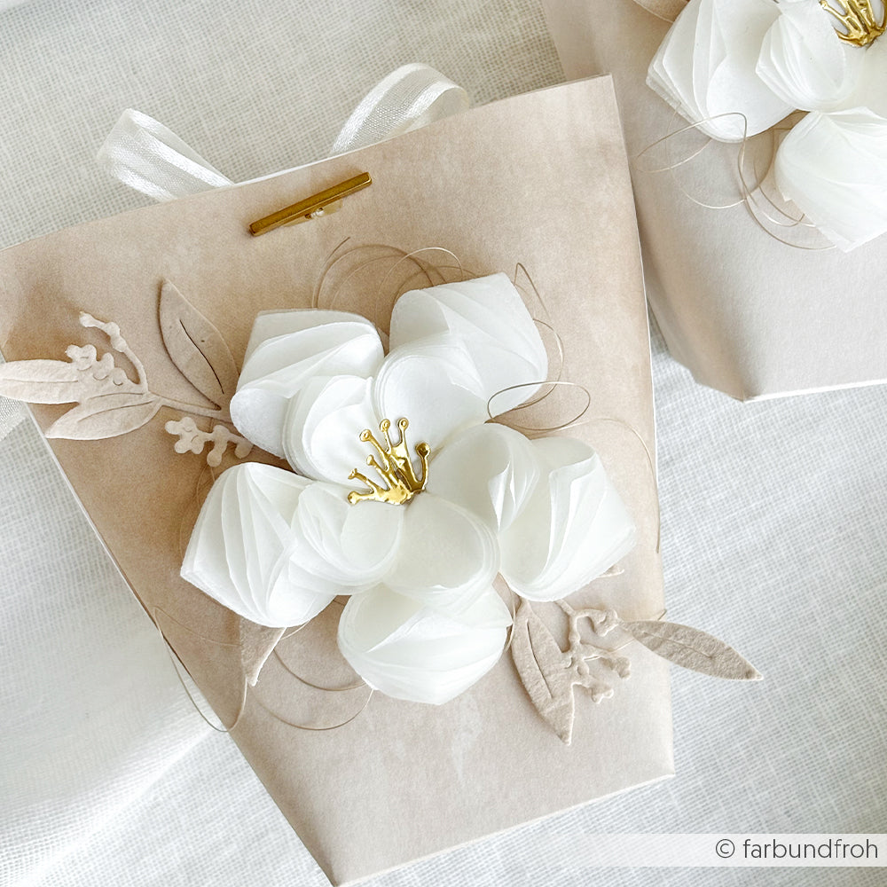 Eine Geschenktüte aus Kraftpapier, verziert mit einer großen weißen Papierblume und beigen Blättern, hergestellt aus Alexandra Renke Designpapier Calm Puderbeige - ideal für einzigartige Papierprojekte oder kreative buchbinderische Akzente.