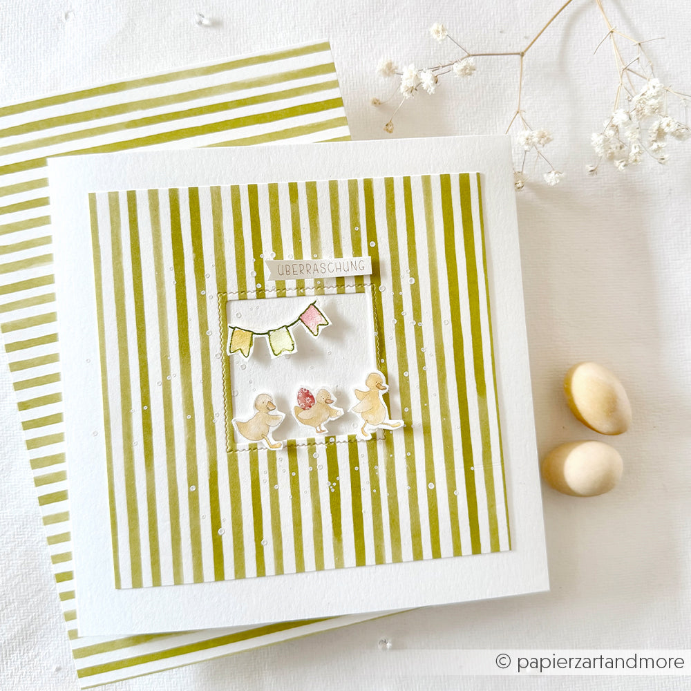 Quadratische Karte von Alexandra Renke mit Streifen Gelbgrün, kleinen Entenküken, Ammern und dem Text "Überraschung" mit Eiern und Blumen - perfekt für Papierprojekte oder zur Kombination mit Ihrem Lieblingsdesignpapier.
