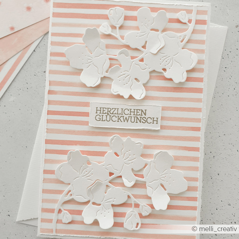 Handgemachte Grußkarte von Alexandra Renke mit weißen Blumen-Ausstanzungen auf korallrosafarbenem Designpapier und "Herzlichen Glückwunsch" in der Mitte - ideal für kreative Papierprojekte.