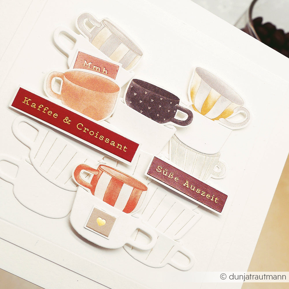 Gestapelte illustrierte Kaffeetassen mit den Aufschriften "Kaffee & Croissant" und "Süße Auszeit" von Alexandra Renke-ideal Designpapier für Papierprojekte, die einen floralen Tassenrapport für kreative Gestaltungsideen präsentieren.