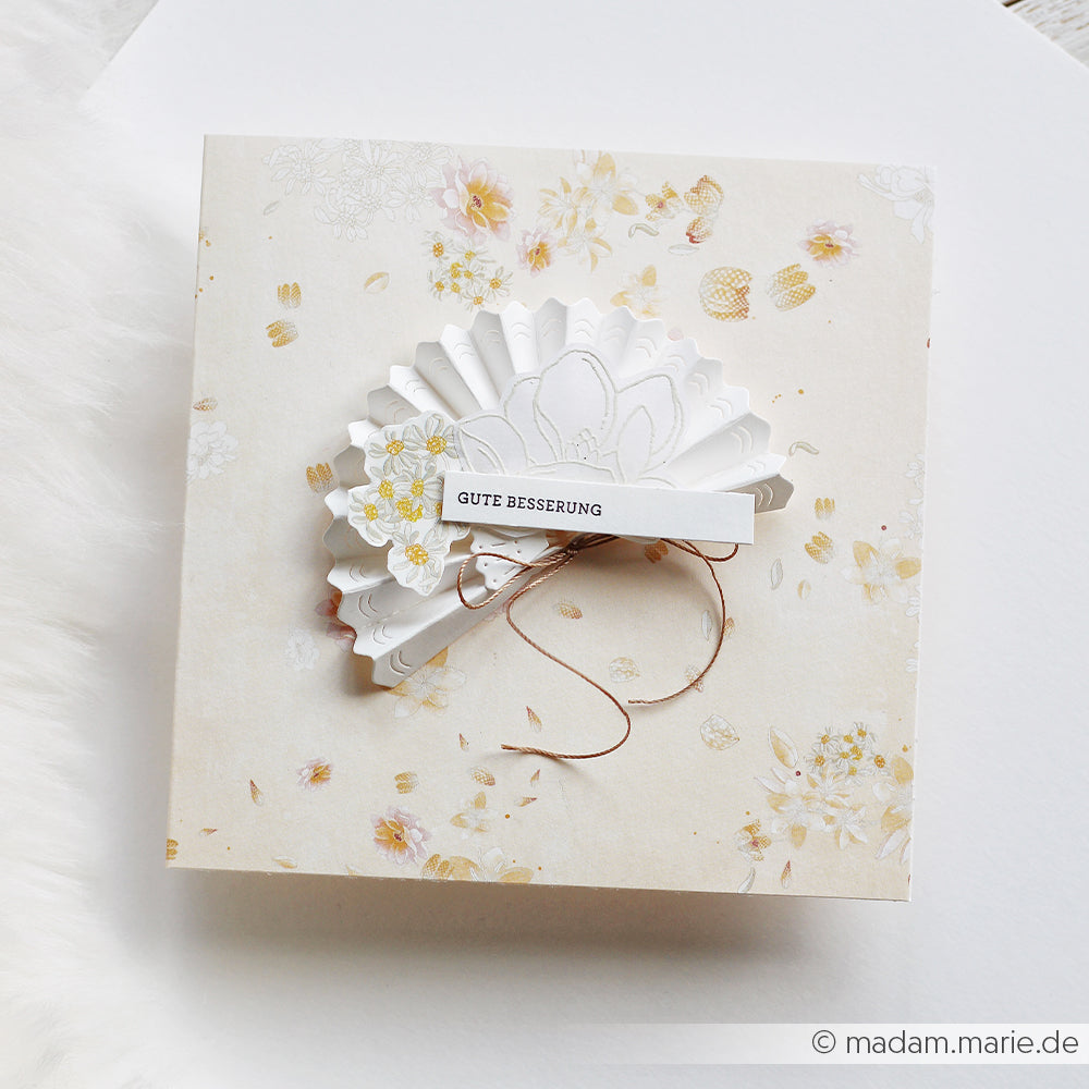 Beigefarbene Blumenkarte von Alexandra Renke mit einem weißen Papierfächer und dem Text "GUTE BESSERUNG", mit einer zarten Blumenkomposition - ideal für Papierprojekte oder als nette Geste.