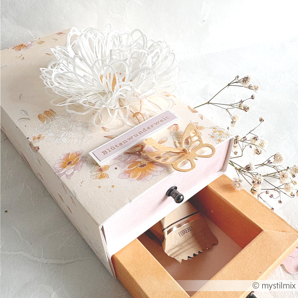 Dekorative Geschenkbox von Alexandra Renke mit einem Blumenarrangement, einer Papierblume, einem ausgeschnittenen Schmetterling, hochwertigem Designpapier und einer aufklappbaren Schublade, hinter der sich ein kleines Geschenk verbirgt.