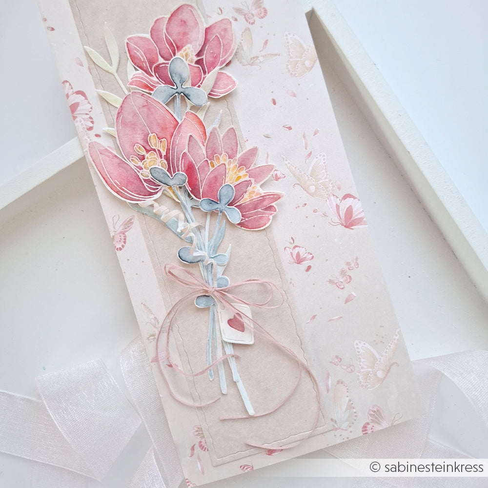 Handgefertigte Karte von Alexandra Renke mit rosa und blauen Papierblumen, einem Band und einer floralen Schmetterlingskomposition auf Designpapier mit Schmetterlingsmuster.