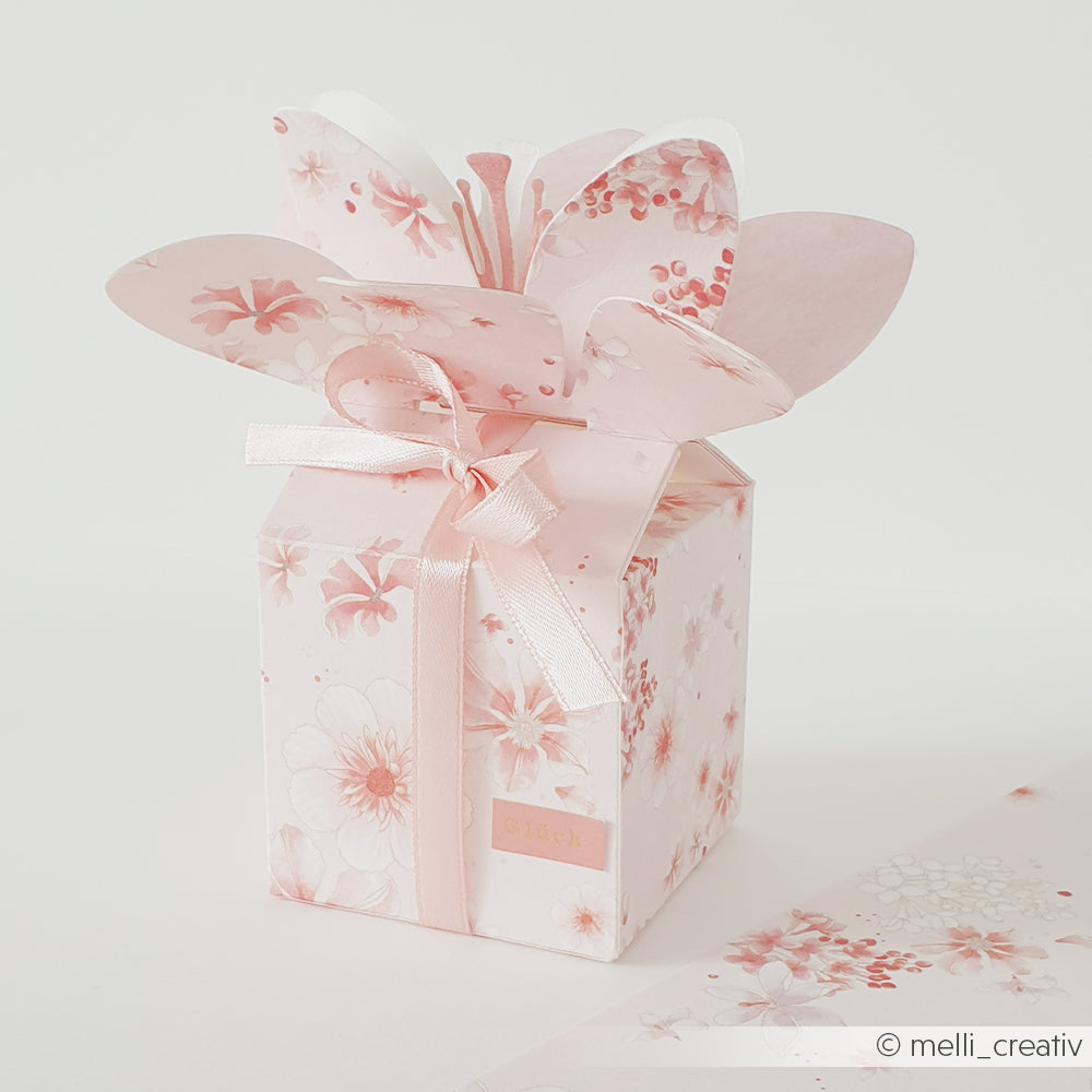 Eine blassrosa Geschenkbox mit Blumenmotiv, verziert mit einer Schleife und einem blütenblattförmigen Deckel sowie zarten Blumenmustern – ein bezauberndes Exemplar von Alexandra Renke mit einer eleganten floralen Blütenkomposition aus exquisitem Designpapier.