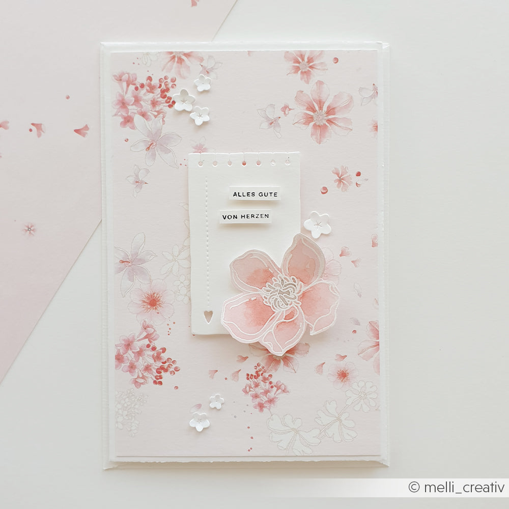 Eine Grußkarte mit Blumenmotiv von Alexandra Renke, verziert mit rosa Blüten und dem deutschen Text „ALLES GUTE VON HERZEN“ auf einem weißen Etikett – ideal für Papierprojekte oder als Inspiration für einzigartige Kreationen aus Designpapier.