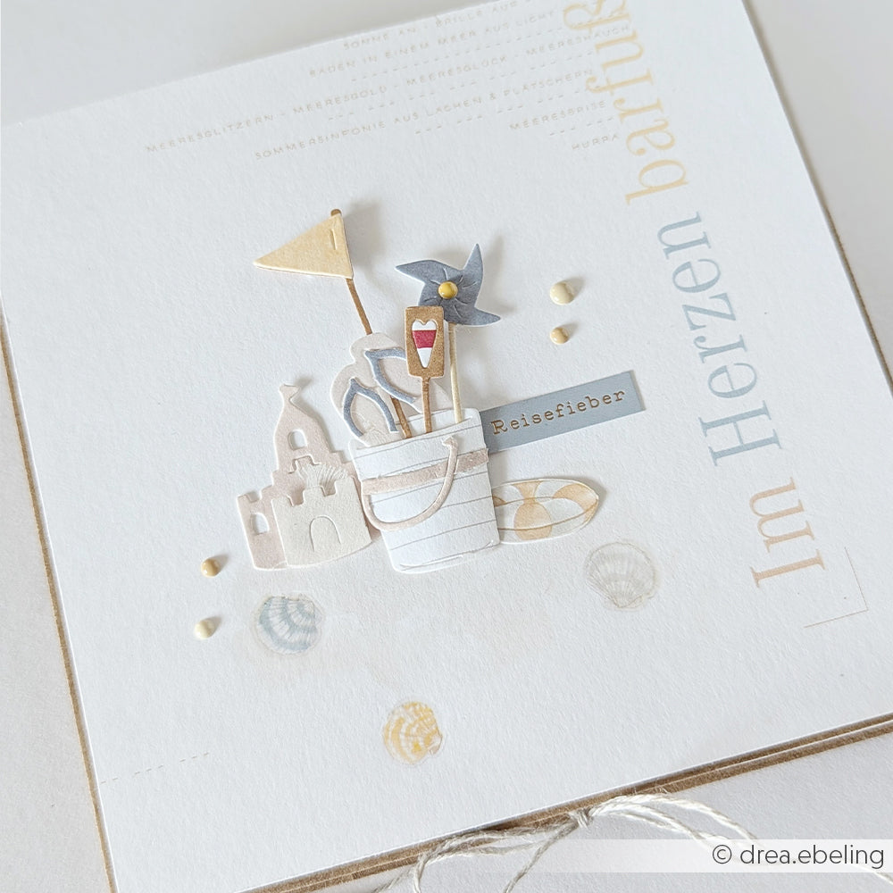 Minimalistische Karte von Alexandra Renke mit Ausschnitten zum Thema Strand – Sandkübel, Windrad, Sandburg und „Reisefieber“ – ideal für Papierprojekte oder um Buchbinderei-Kreationen das gewisse Etwas zu verleihen.