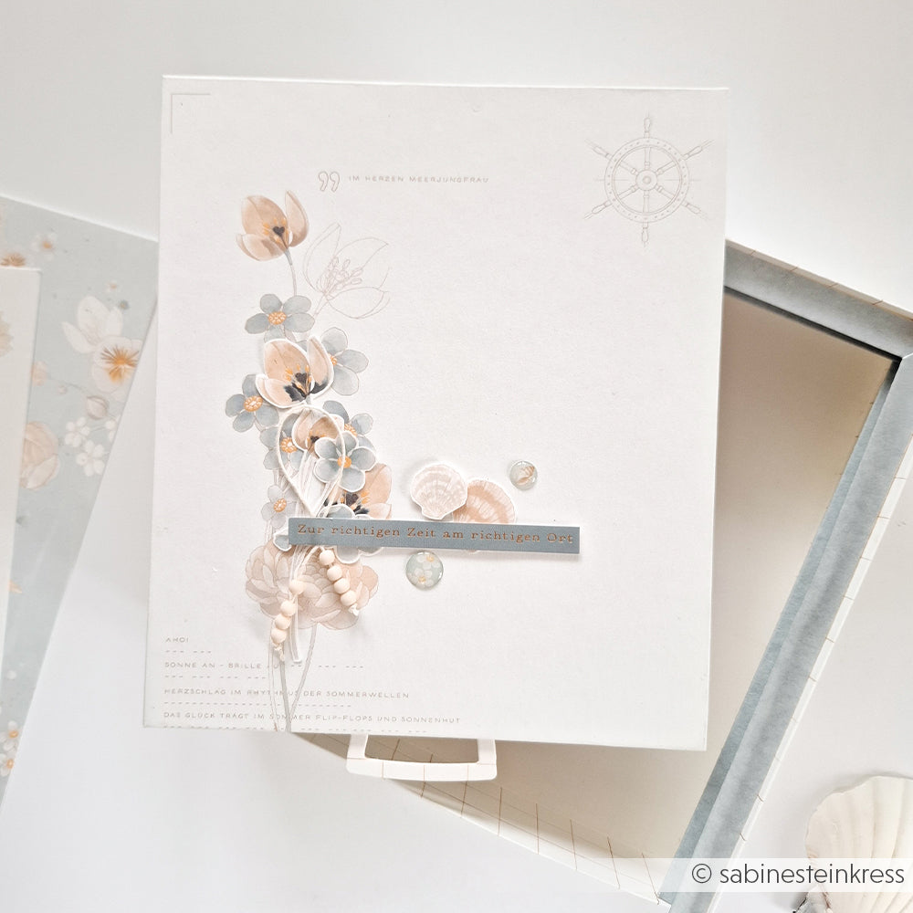 Eine Blumenkarte von Alexandra Renke mit zartbeigen Blumen auf hochwertigem Designpapier mit deutschem Text, dargestellt auf einem Leuchtkasten.