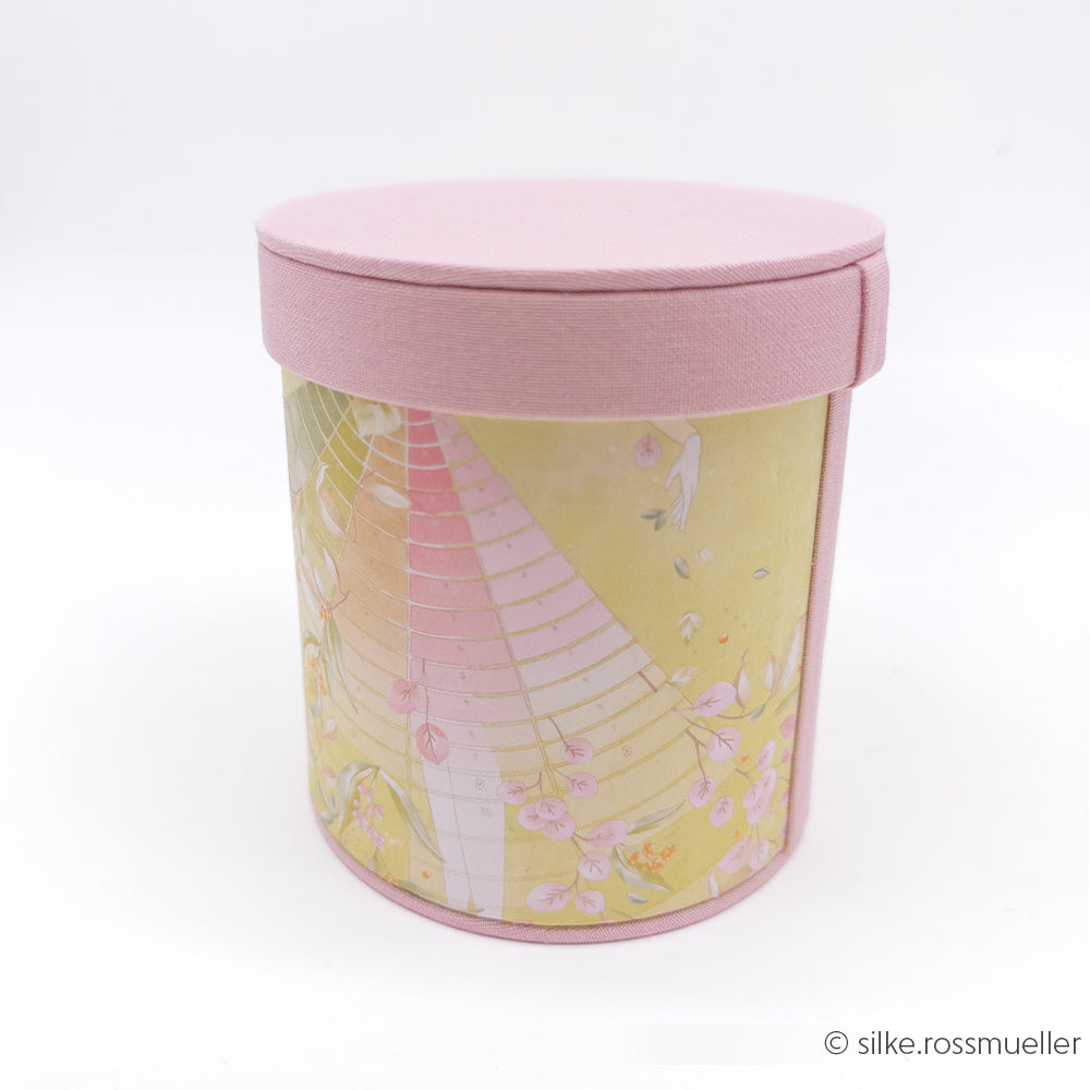 Runde rosa Geschenkbox von Alexandra Renke mit einem Blumenmuster auf hochwertigem Designpapier vor einem zarten Pastellhintergrund – ideal für Papierprojekte oder als Teil einer Dekoration mit floralen Gartenfiguren.