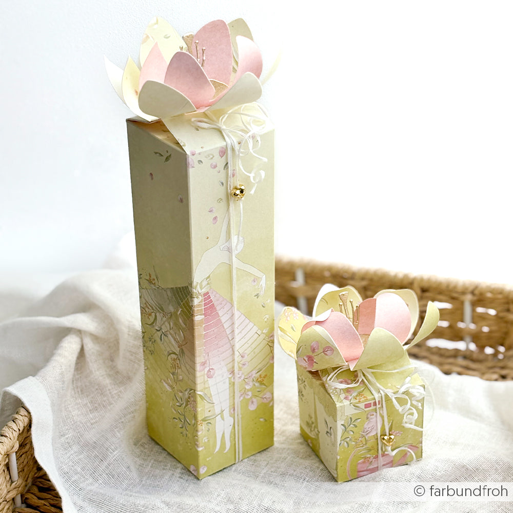 Zwei pastellfarbene Geschenkboxen mit Deckeln aus Papierblumen, gefertigt aus exquisitem Designpapier von Alexandra Renke und verziert mit einer zarten Illustration eines Mädchens in einem rosa Kleid – perfekt für bezaubernde Papierprojekte, die von einem blumigen Garten inspiriert sind.