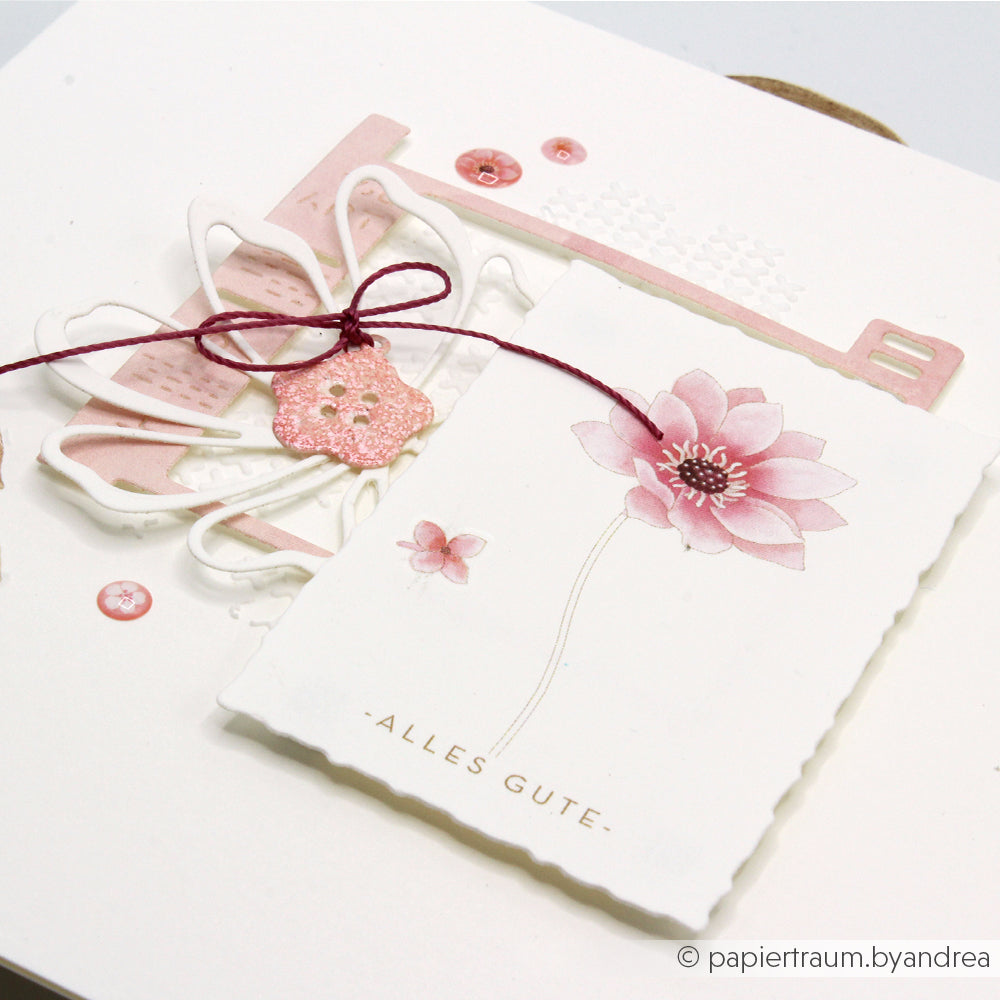 Eine handgefertigte Karte aus dem „Floraler Kärtchenbogen Rosa“-Designpapier von Alexandra Renke, mit einer rosa Blume, dem Schriftzug „Alles Gute“ auf Deutsch, rosa Akzenten, einer gebundenen Schleife und einem Glitzerknopf – ideal für Papierprojekte.