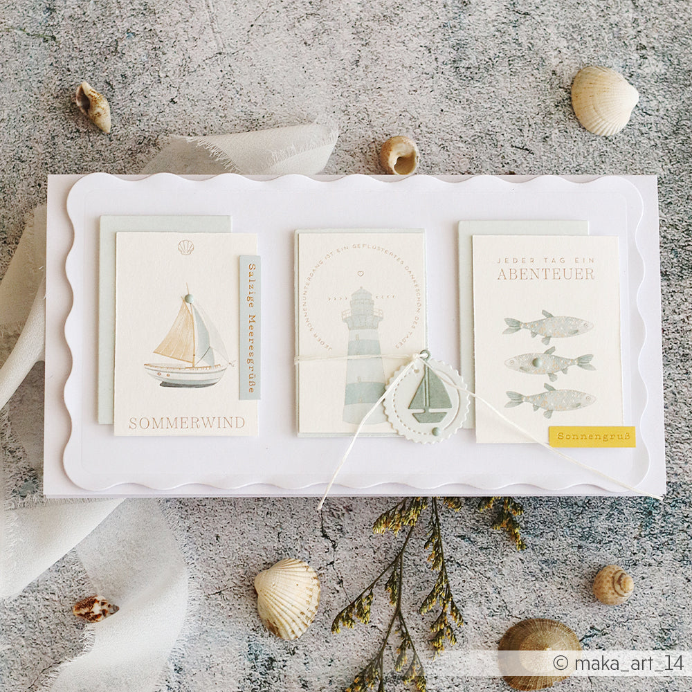Ein Set aus drei Karten im maritimen Stil von Alexandra Renke, gefertigt aus Designpapier und verziert mit Muscheln, Blumen und einem Segelboot-Anhänger. Ideal für Papierprojekte oder als Akzent in einem floralen Kärtchenbogen.