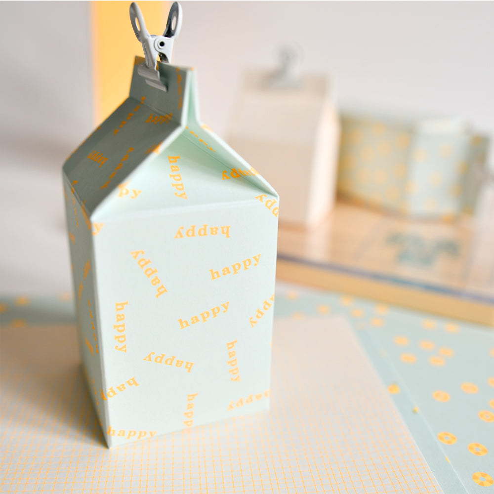 Hellblauer Neon-Papierkarton mit dem gelb aufgedruckten Wort „happy“, oben abgeschnitten, auf einem pastellfarbenen Schreibtisch – perfekt für kreative Papierprojekte und stilvolle Designpapier-Präsentationen.