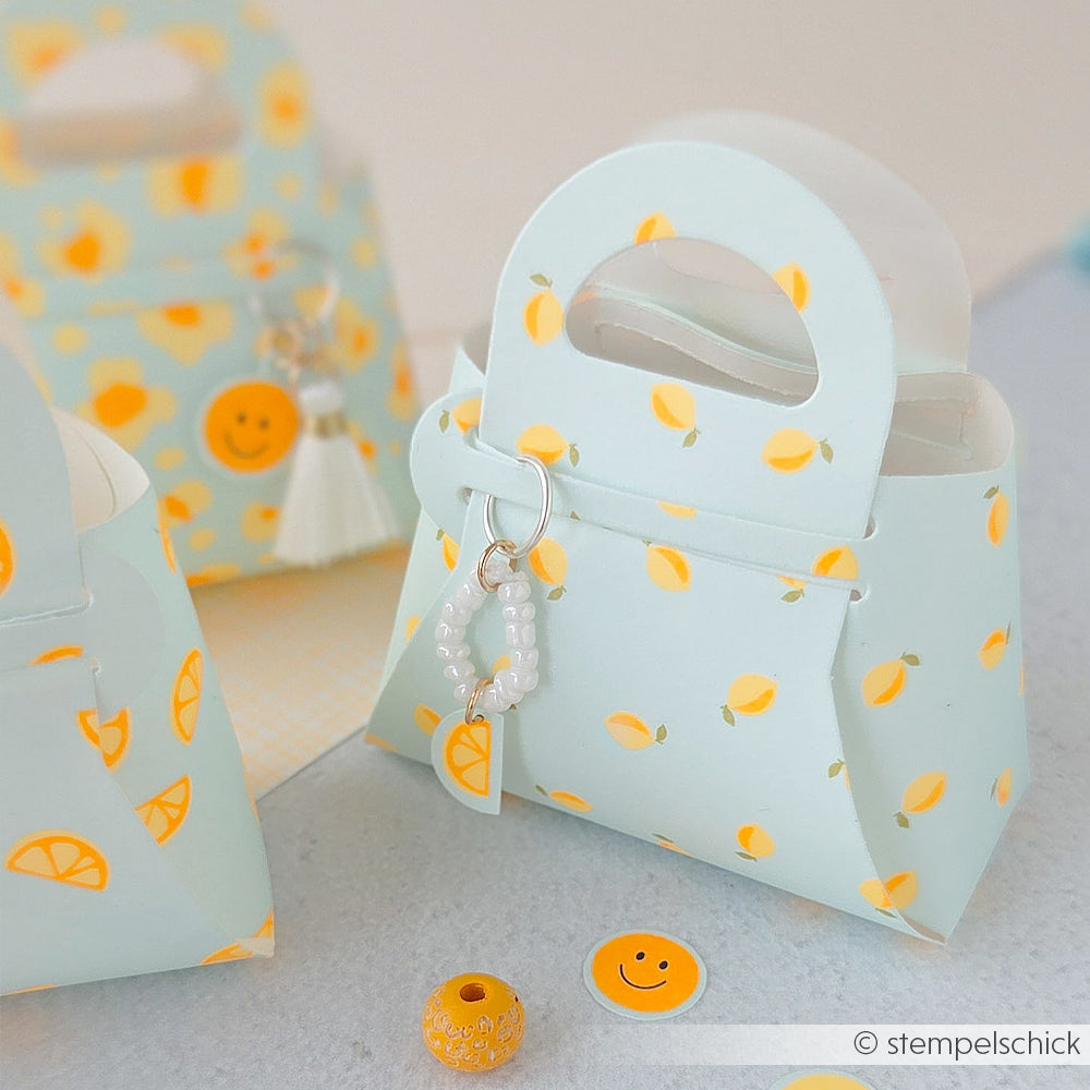 Kleine pastellfarbene Geschenktüten mit Zitronenmuster aus hochwertigem Designpapier, verziert mit einem weißen Perlenanhänger und Smiley-Konfetti – eine bezaubernde Idee von Papierprojekte, perfekt für Ihre „Sommer Special Zitronen“-Feierlichkeiten.
