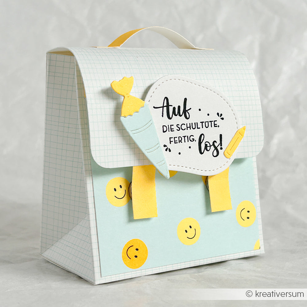 Papierrucksack mit gelben Henkeln, Smileys und deutschem Text, gefertigt aus Neon-Papier und verziert mit einer Papiermöhre und einem Bleistift – eine perfekte Ergänzung für deine Papierprojekte.